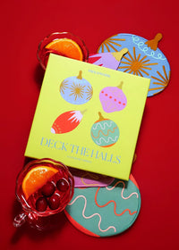 A bright yellow-green deck of cards titled "Deck the Halls" by Jack Cohen, styled on a red background with colorful holiday-themed coasters and drinks.