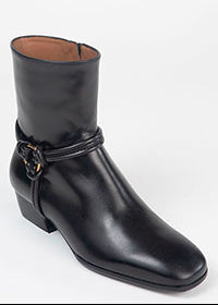 A black leather ankle boot with a low block heel and a decorative strap detail on the side, photographed against a plain white background.