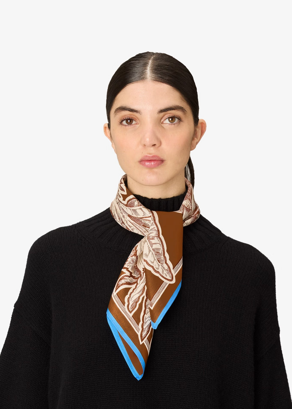 A woman with dark hair pulled back wears a black knit sweater and a patterned silk scarf. The scarf features a brown and beige botanical design with bright blue edges, shown against a plain light gray background.