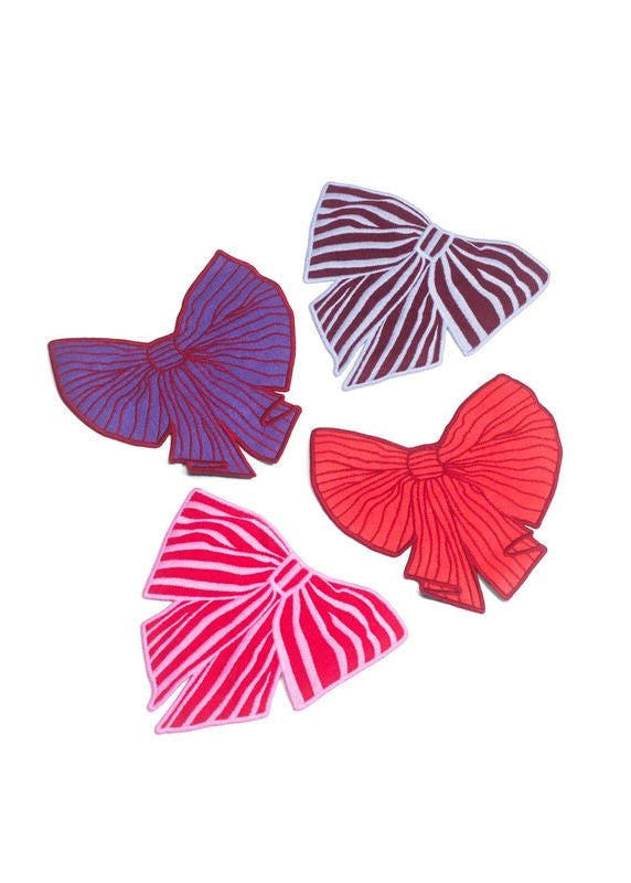 Four embroidered bow cocktail napkins in purple, burgundy, red, and pink, arranged on a plain white background.