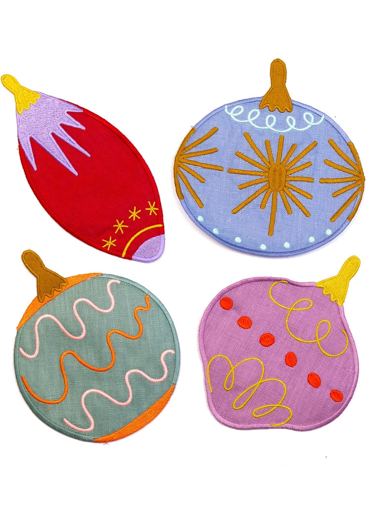 Four colorful embroidered ornament cocktail napkins arranged in a 2x2 grid on a plain white background. The ornaments have whimsical shapes and patterns in red, lavender, mint green, and pink, with yellow, orange, and purple embroidery details.