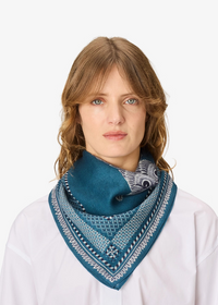 A woman with light brown hair wearing a white shirt and a teal blue patterned bandana scarf, photographed against a solid white background.