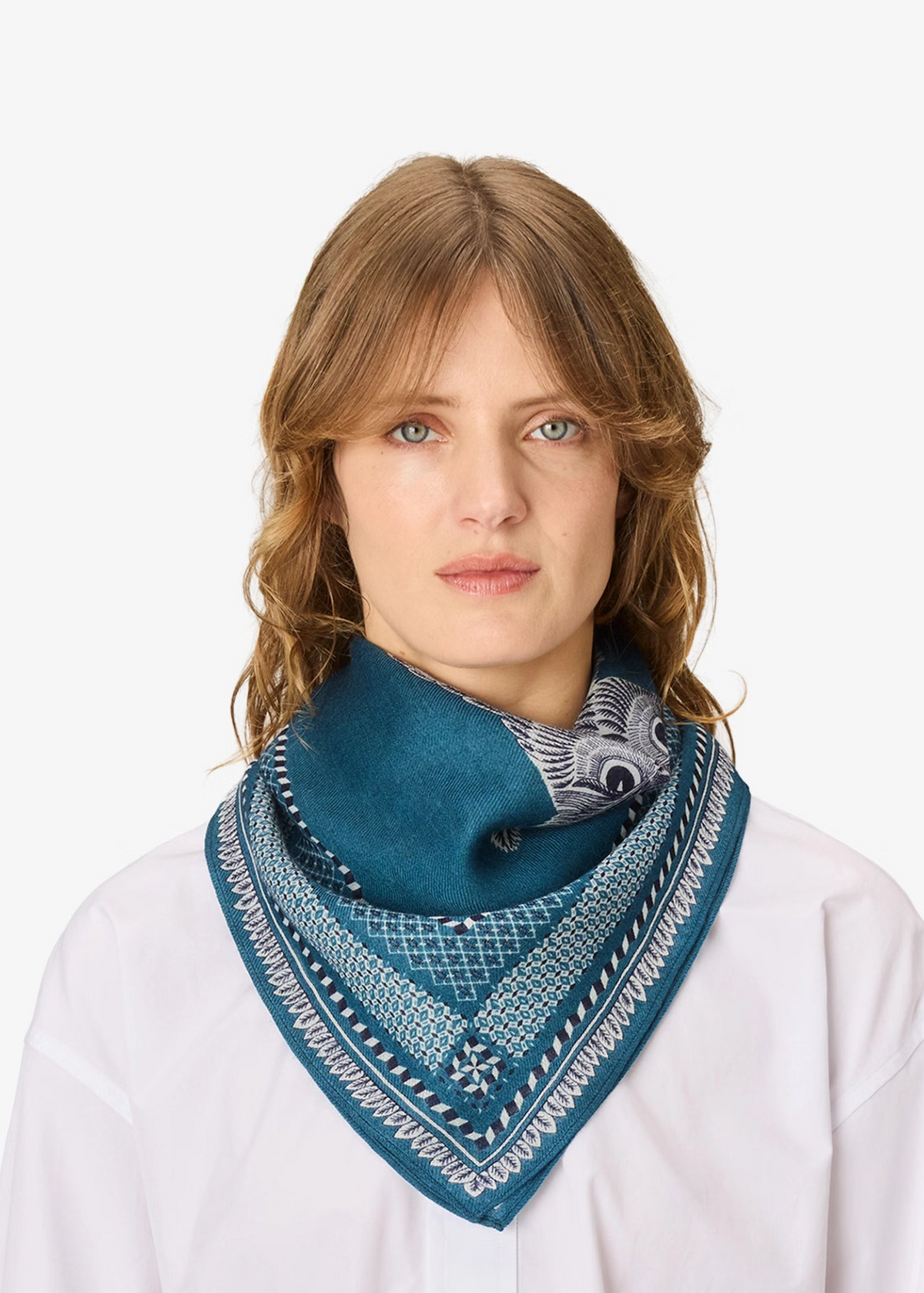 A woman with light brown hair wearing a white shirt and a teal blue patterned bandana scarf, photographed against a solid white background.