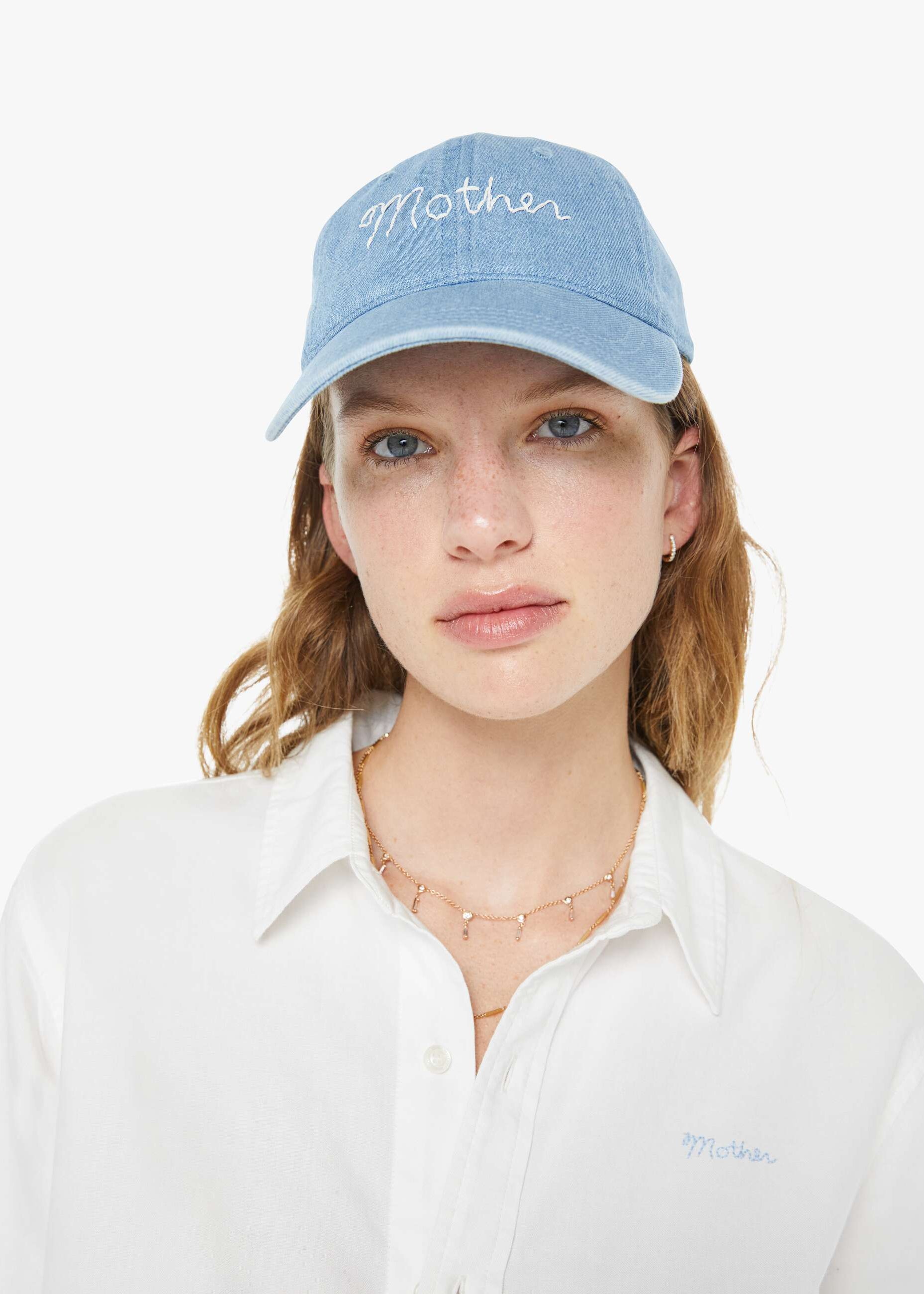 Woman wearing a light blue cap with 'Mother' embroidered on it against a white background