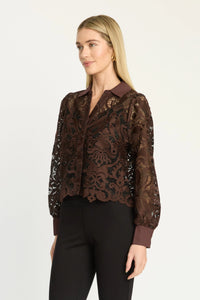 A woman modeling a brown lace long-sleeve blouse with a scalloped hem and dark brown collar, paired with black pants, against a plain light gray studio background.