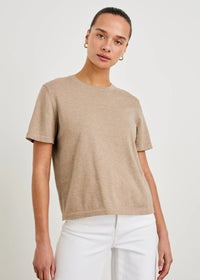 Woman wearing a beige t-shirt and white pants on a plain background