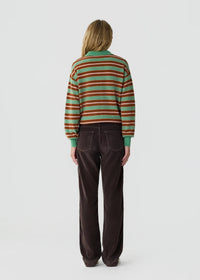 A model viewed from the back wearing a green, brown, and red striped knit sweater and dark brown corduroy trousers, set against a plain light gray studio background.