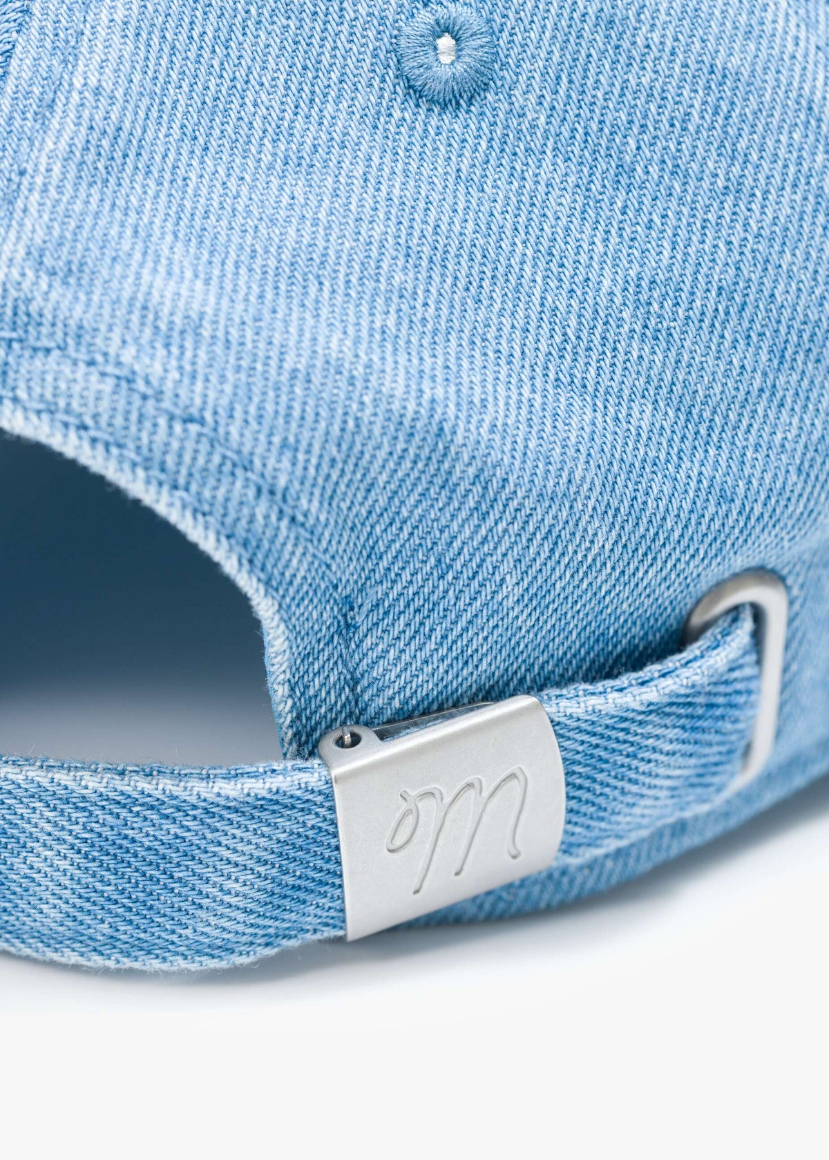 Close-up of a blue denim cap with a metal brand tag on a white background