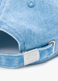 Close-up of a blue denim cap with a metal brand tag on a white background