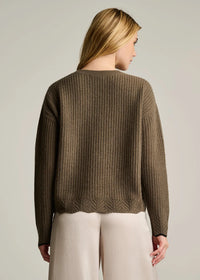 Woman wearing a brown textured sweater and light-colored pants against a plain background