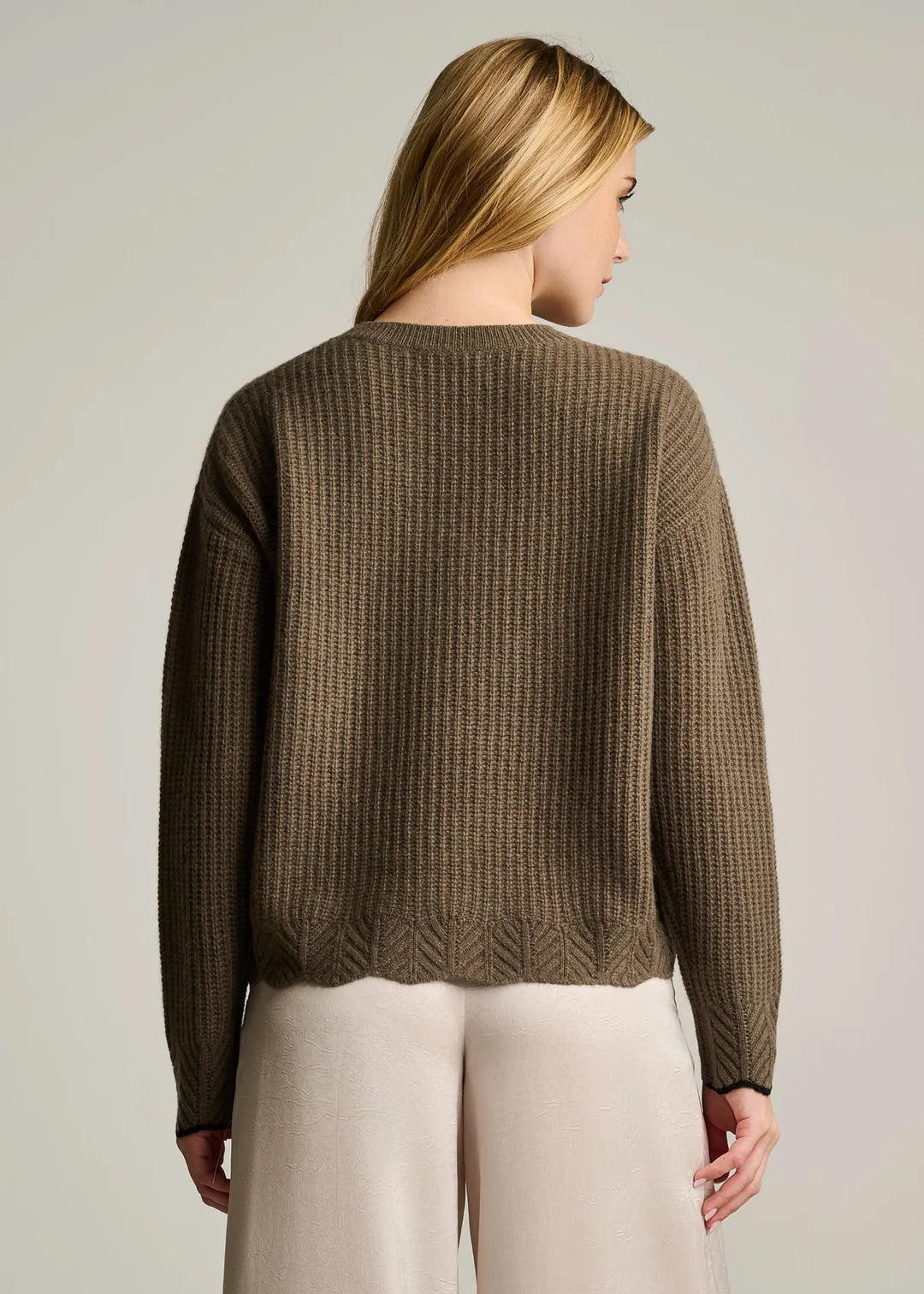 Woman wearing a brown textured sweater and light-colored pants against a plain background