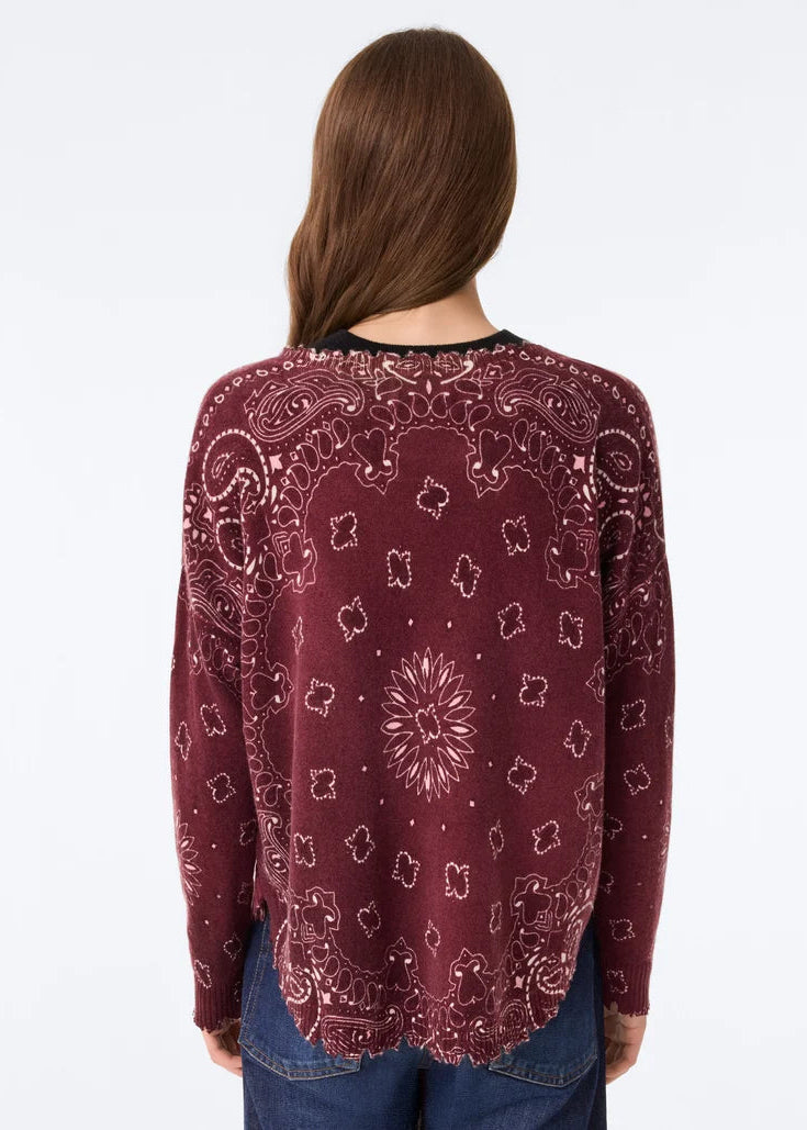 A woman viewed from behind wearing a long-sleeve maroon knit top with a white paisley bandana print, paired with blue jeans, against a plain white background.