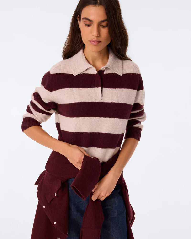 A woman wearing a knit polo sweater with horizontal burgundy and cream stripes, styled with a matching burgundy jacket tied around her waist and blue jeans, against a plain white studio background.