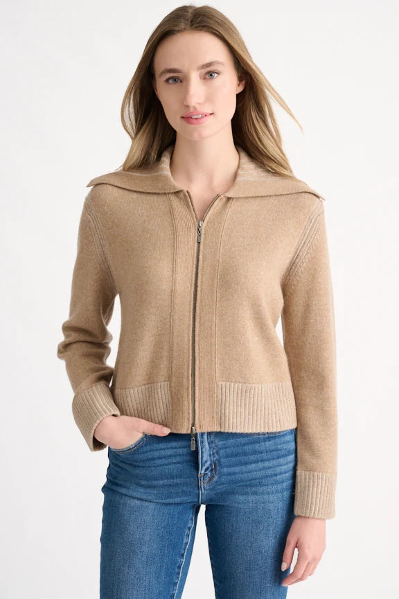 Woman wearing a beige zip-up sweater and blue jeans on a white background