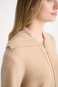 Close-up side view of a woman wearing a beige knit zip-front top with a wide collar and subtle textured stripe details on the shoulder.