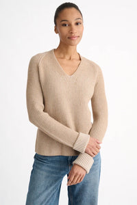 Woman wearing a beige sweater and blue jeans on a white background