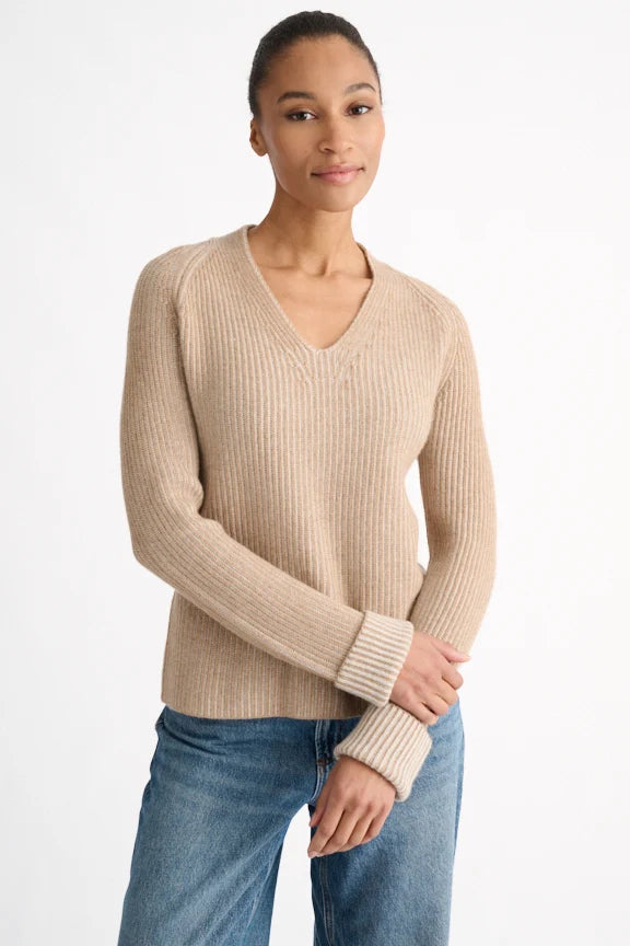 Woman wearing a beige sweater and blue jeans on a white background