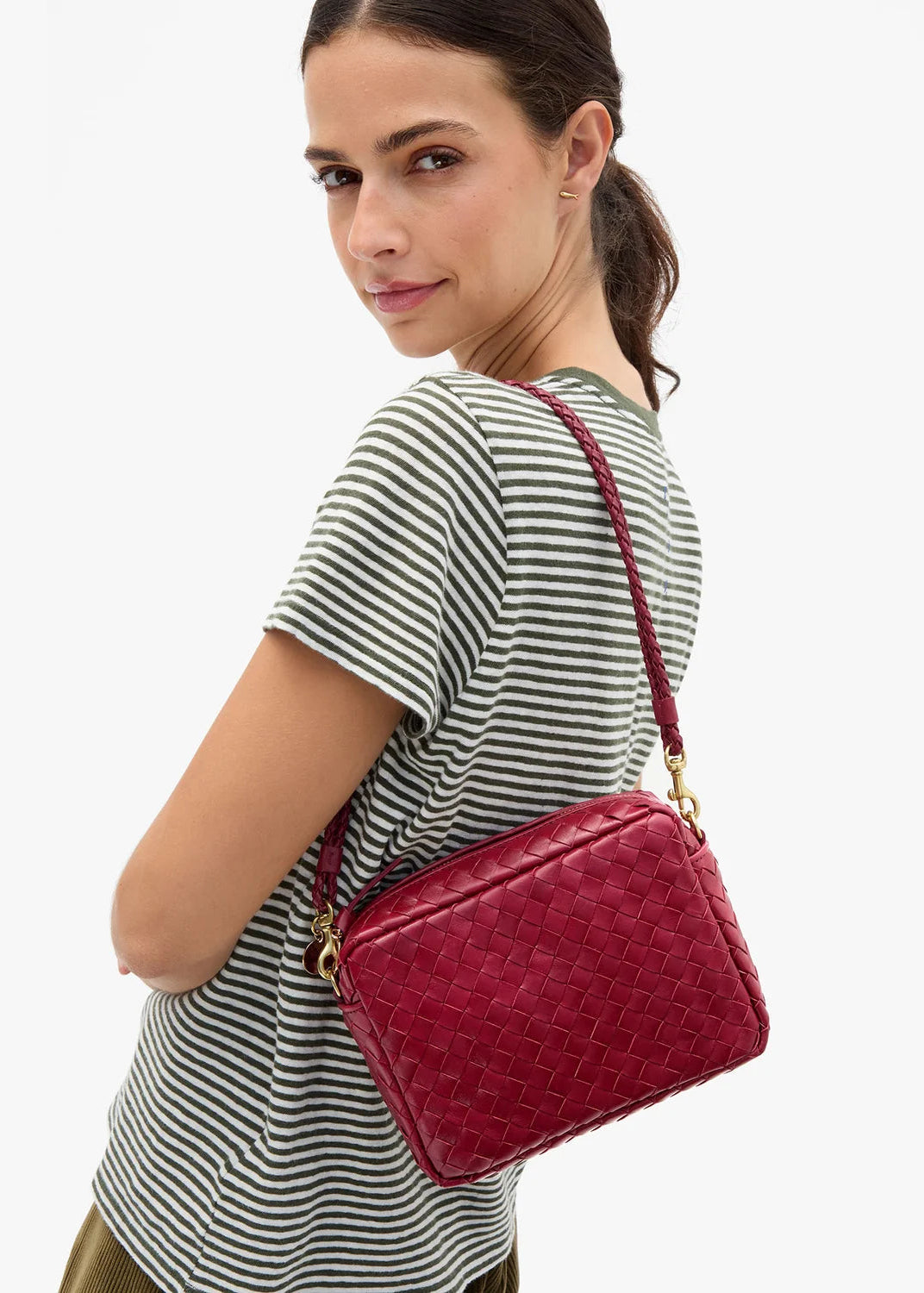 A woman wearing a striped t-shirt models a red woven leather crossbody bag with gold hardware against a plain white background.