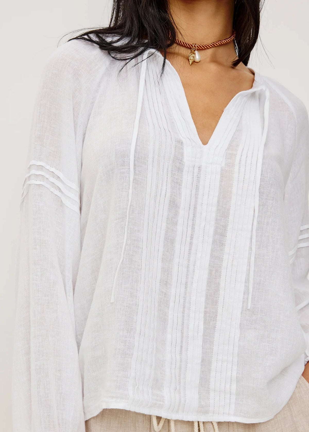 White blouse with pleated details worn by a person, against a neutral background
