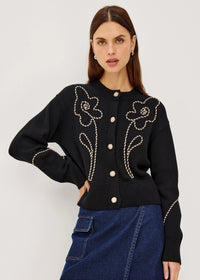 Woman wearing a black embroidered jacket and denim skirt on a white background