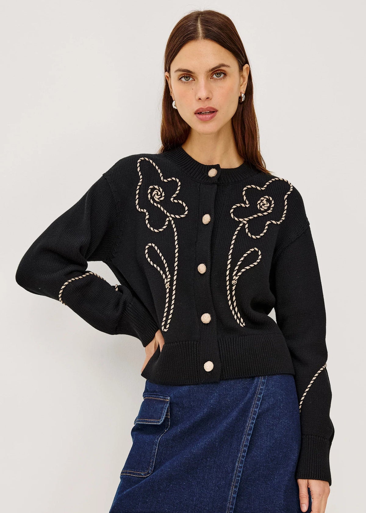 Woman wearing a black embroidered jacket and denim skirt on a white background