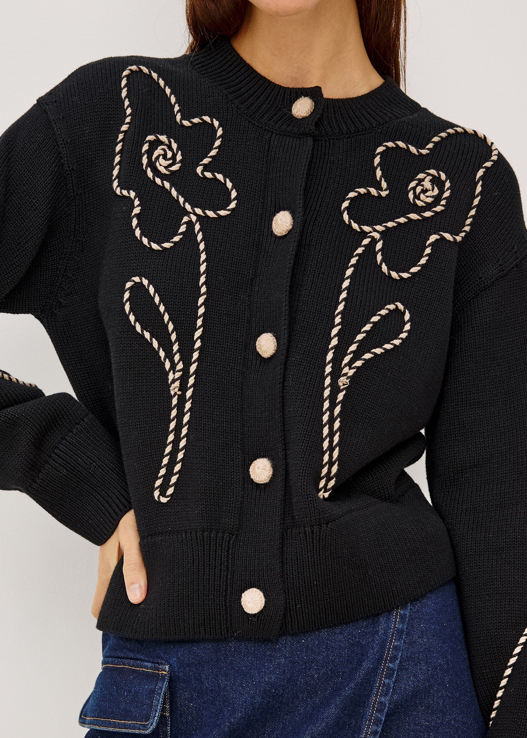 Black cardigan with floral embroidery on a plain background