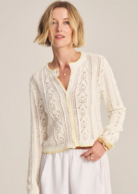 Woman wearing a cream-colored lace cardigan against a plain background