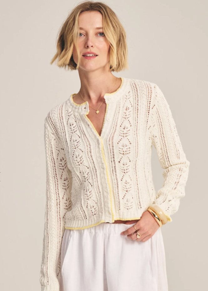 Woman wearing a cream-colored lace cardigan against a plain background