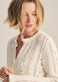 Woman wearing a cream-colored knit cardigan against a plain background