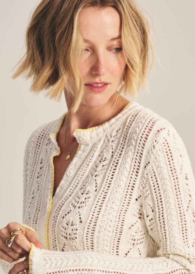 Woman wearing a cream-colored knit cardigan against a plain background