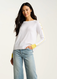 Woman wearing a white sweater with yellow accents and striped pants on a plain background