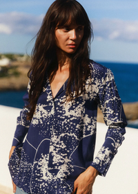 Woman wearing a blue and white patterned shirt by the ocean