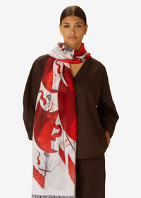 Woman wearing a long, patterned scarf with red and white design on a plain background