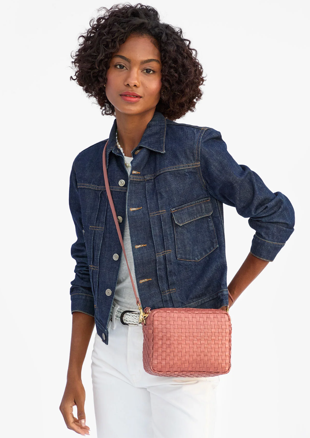 Woman wearing a denim jacket with a pink quilted handbag on a white background