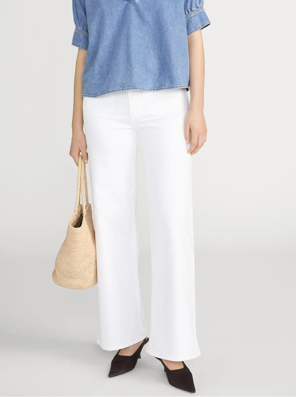 Person wearing a blue shirt, white pants, and holding a straw bag on a plain background