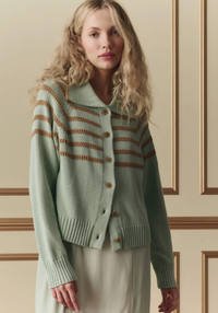 Woman wearing a light green cardigan with brown stripes against a neutral wall.