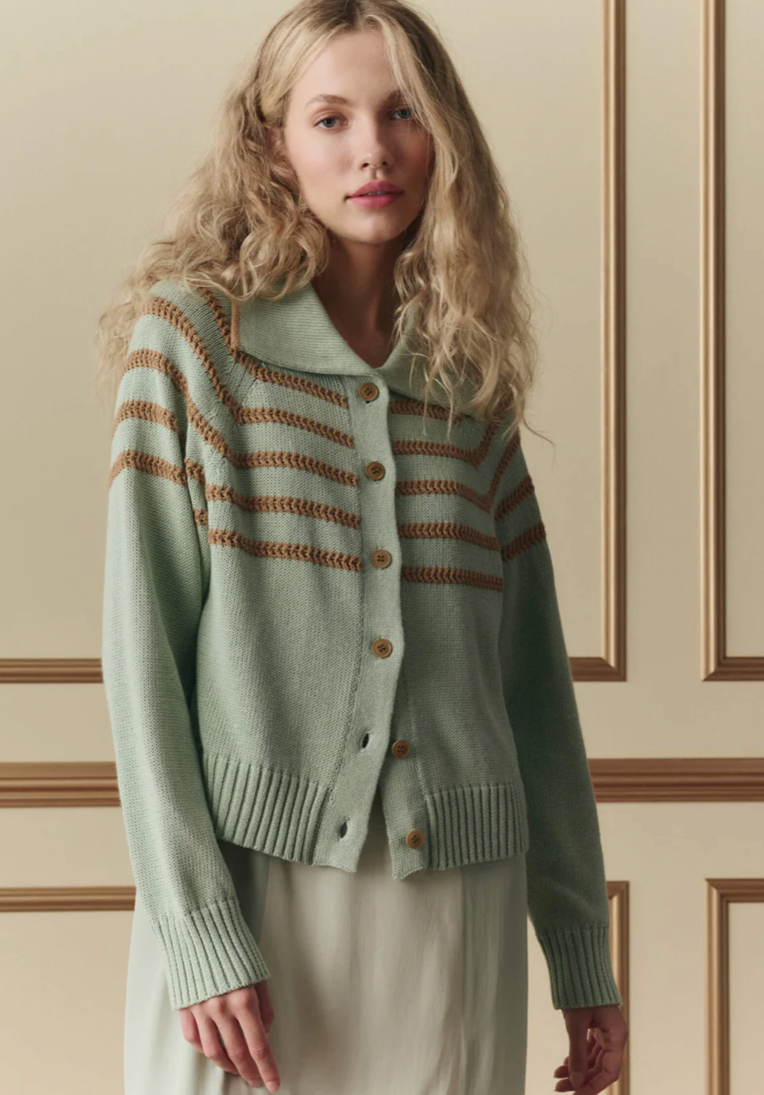 Woman wearing a light green cardigan with brown stripes against a neutral wall.