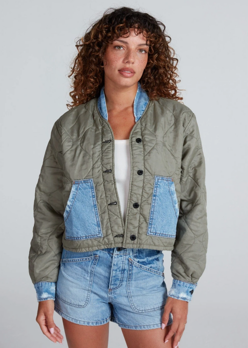 Woman wearing a green jacket with denim accents on a plain background