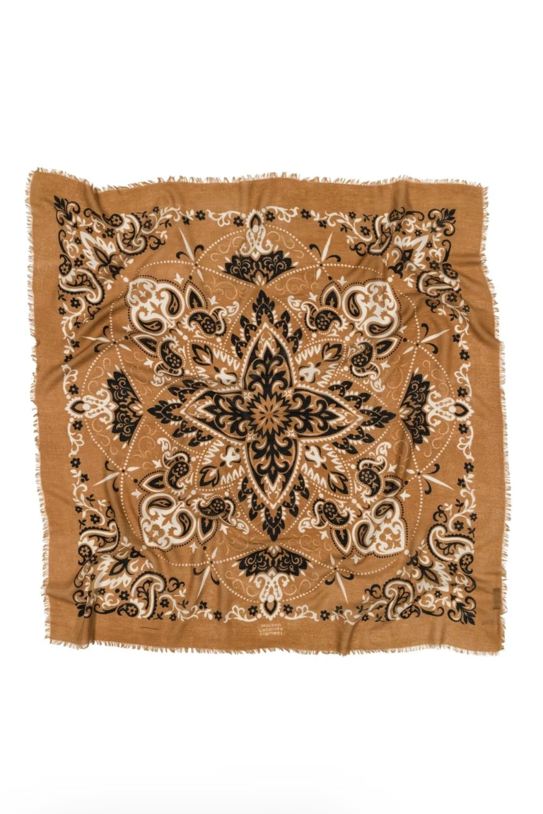 A square scarf with fringed edges, featuring an intricate symmetrical mandala and paisley pattern in black, beige, and brown on a tan background, laid flat against a white background.