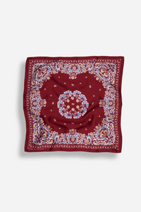 A square red bandana featuring an intricate traditional floral and paisley pattern in blue, beige, and gold, displayed flat against a light gray background.