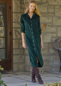 A woman stands on a stone patio wearing a dark green velvet button-front midi dress with long sleeves and a front slit, paired with brown suede boots.