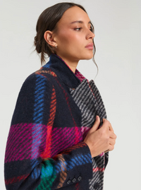 A woman in profile wearing a dark navy wool coat with a vibrant multicolor plaid pattern in pink, red, blue, and green, paired with a gray and black houndstooth scarf.