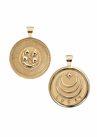 Two gold-toned round pendant charms shown on a plain white background, one displaying a raised three-eyed symbol in a sunburst design and the other showing a crescent moon and star design with the word 'LUCKY' at the bottom.
