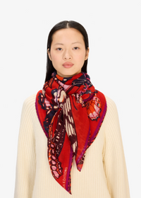 A model wearing a cream ribbed knit sweater and a vibrant red silk scarf with a butterfly print and 'LOEUF RIVOLIERS' text, set against a plain light gray background.