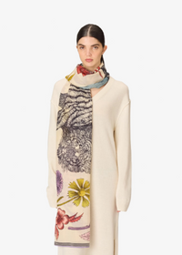 A model wearing a cream-colored knit cardigan and a long cream scarf with a tiger and floral print, set against a plain light gray background.