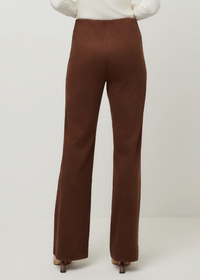 A person shown from the back wearing high-waisted, wide-leg brown pants with a white ribbed top and brown heels, against a plain light gray studio background.