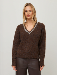 A woman modeling a brown fuzzy knit V-neck sweater with a silver beaded embellishment along the neckline, paired with dark brown pants, against a plain light gray studio background.