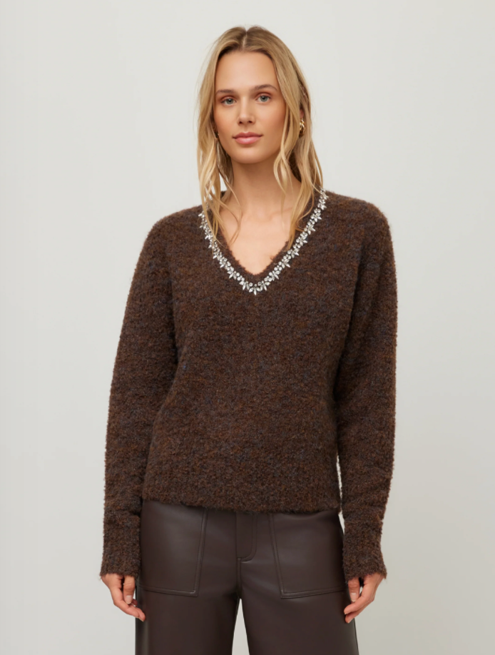 A woman modeling a brown fuzzy knit V-neck sweater with a silver beaded embellishment along the neckline, paired with dark brown pants, against a plain light gray studio background.