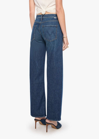 Rear view of a model wearing dark blue wide-leg denim jeans with a tied cream top and navy heels, set against a plain white studio background.