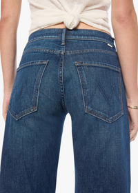 Rear view of a person wearing blue denim jeans with a cream tied top, shown against a plain light background.